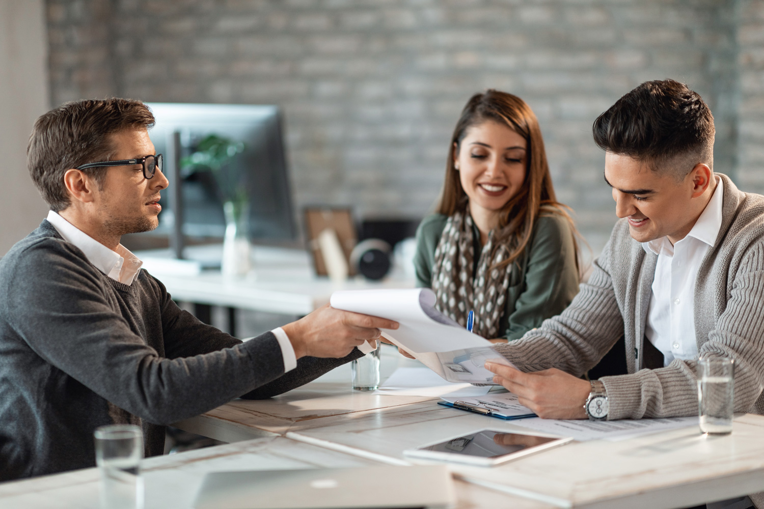 Young smiling couple signing a contract while having meeting with bank manager.