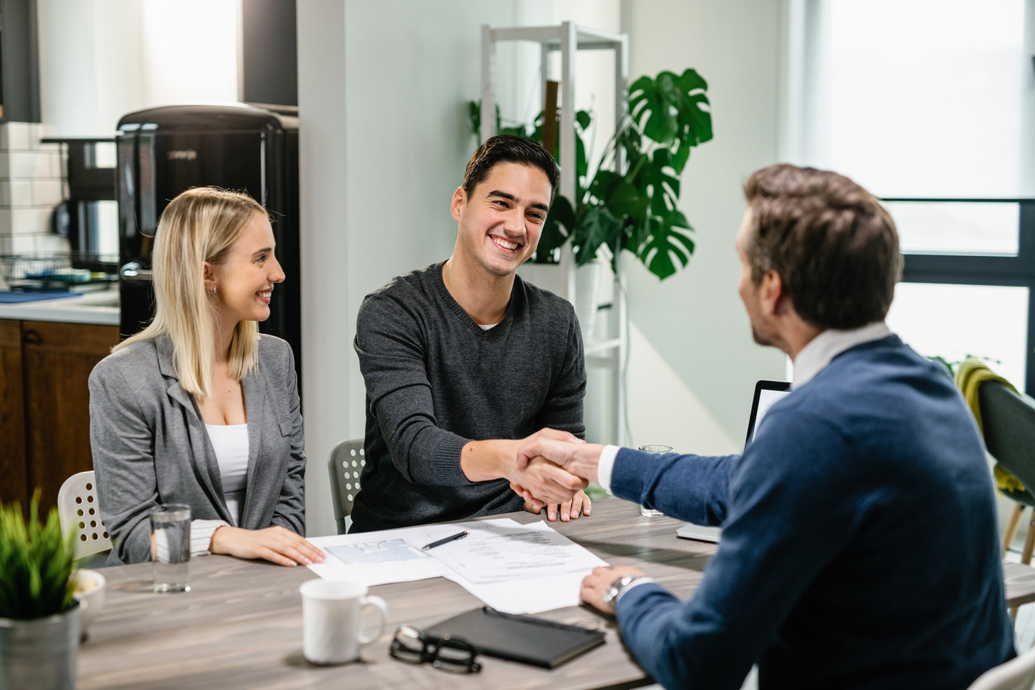 Young smiling couple signing a contract while having meeting with bank manager.